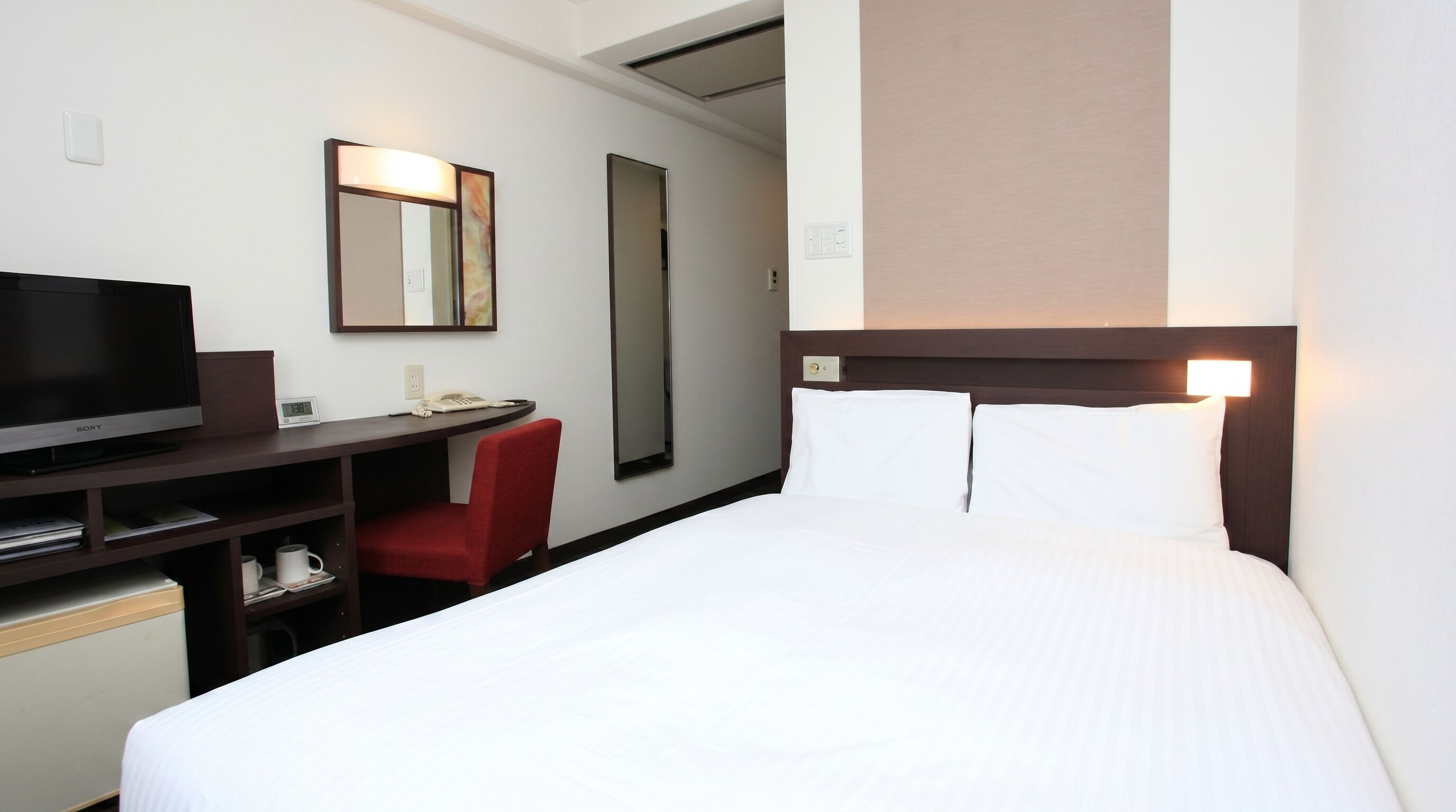 Une chambre d’hôtel avec un lit, un bureau avec une télévision, une chaise et un miroir.