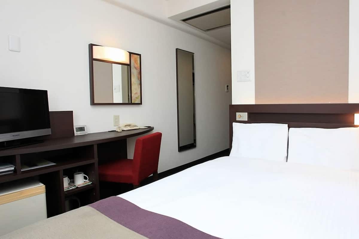 A hotel room with a bed, a desk with a TV, a chair, and a mirror.