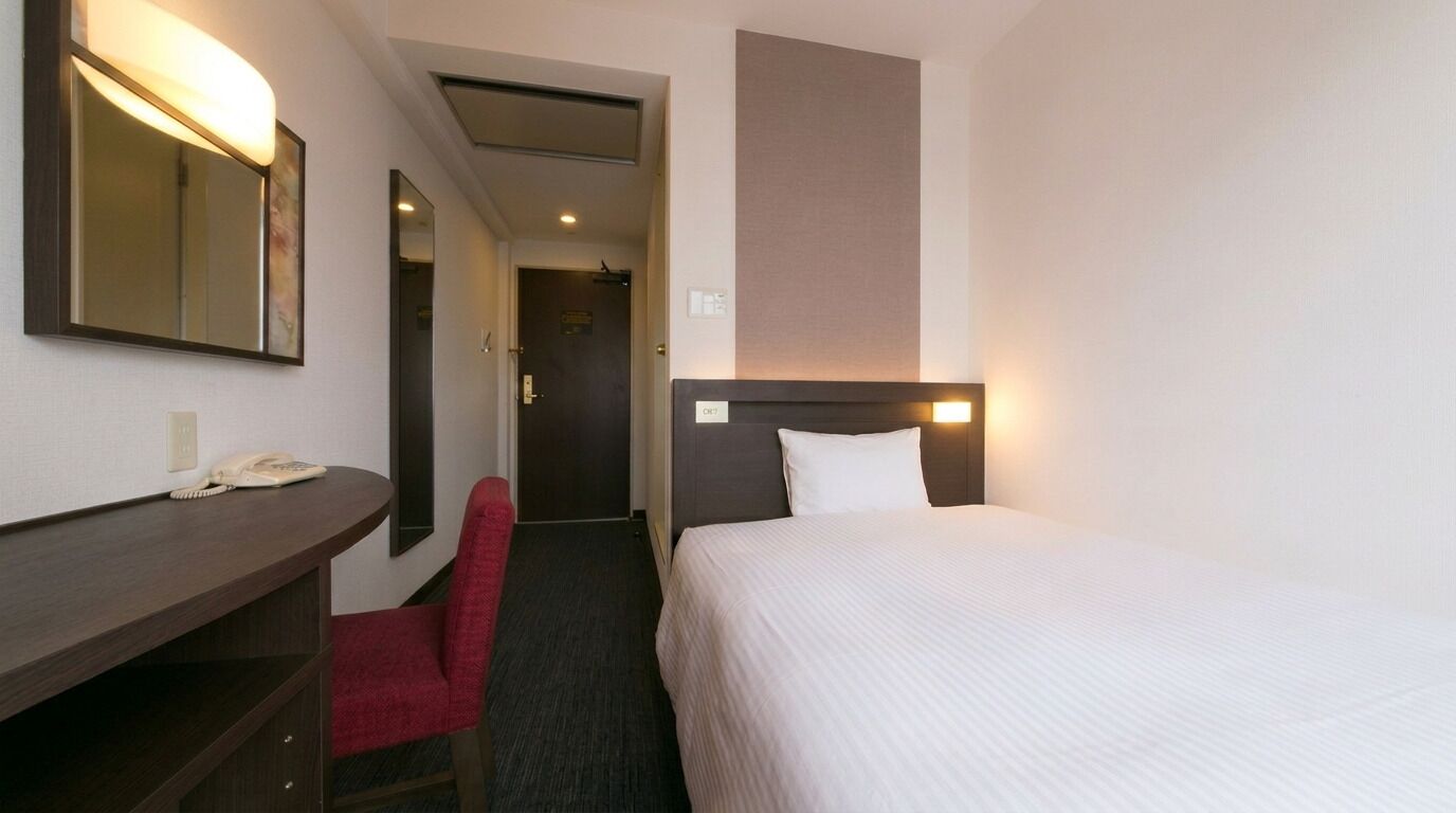 Une chambre d’hôtel avec un lit, un bureau avec un téléphone, une chaise rouge et un miroir.