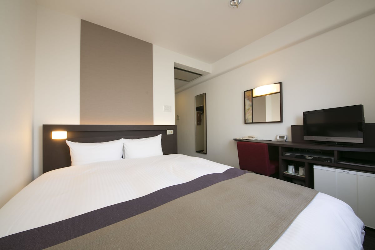 A hotel room with a large bed, a flat-screen TV, a small desk, and a mirror.