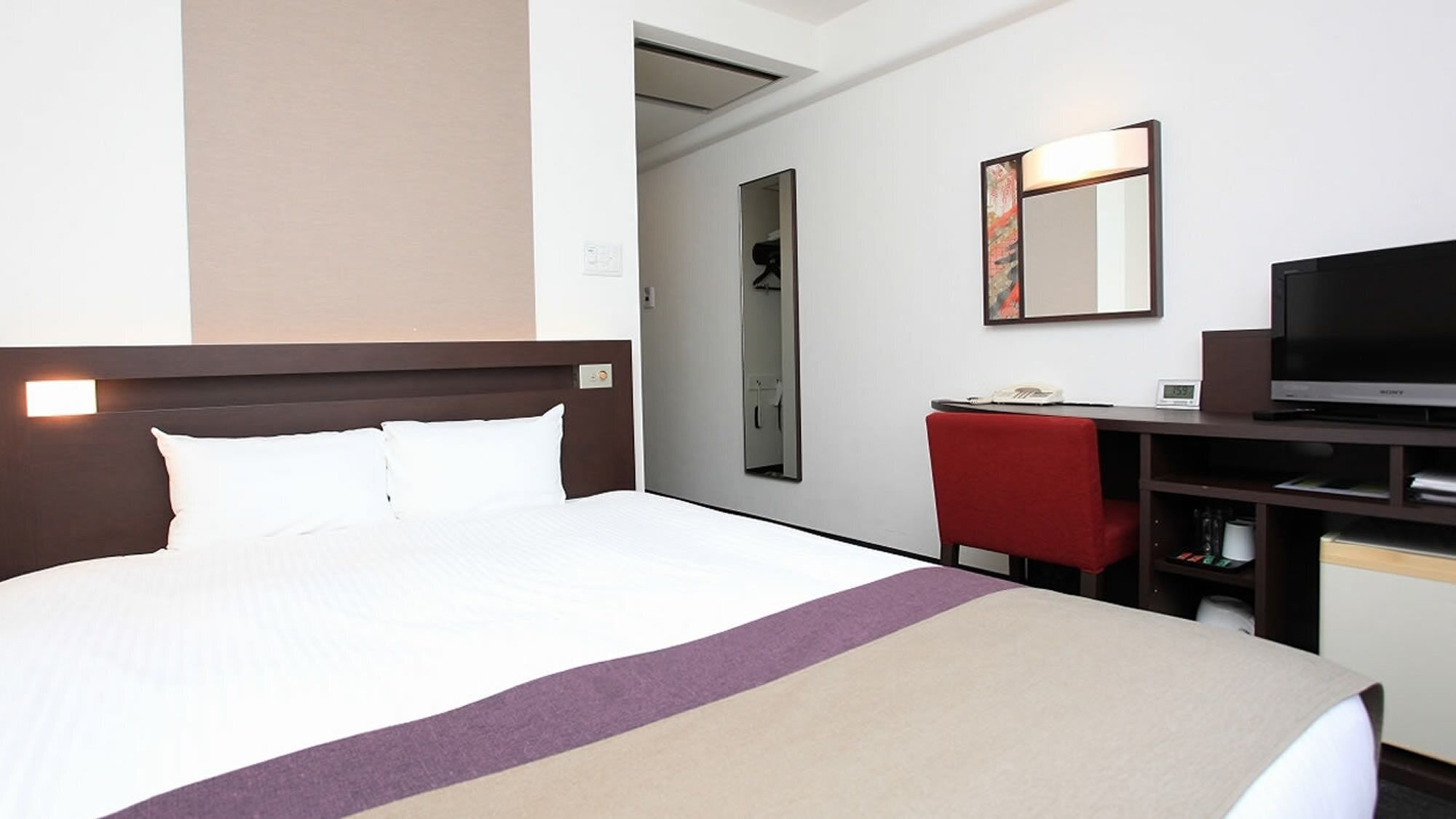 Una camera d'albergo con un letto grande, una scrivania con una sedia, una televisione e uno specchio.