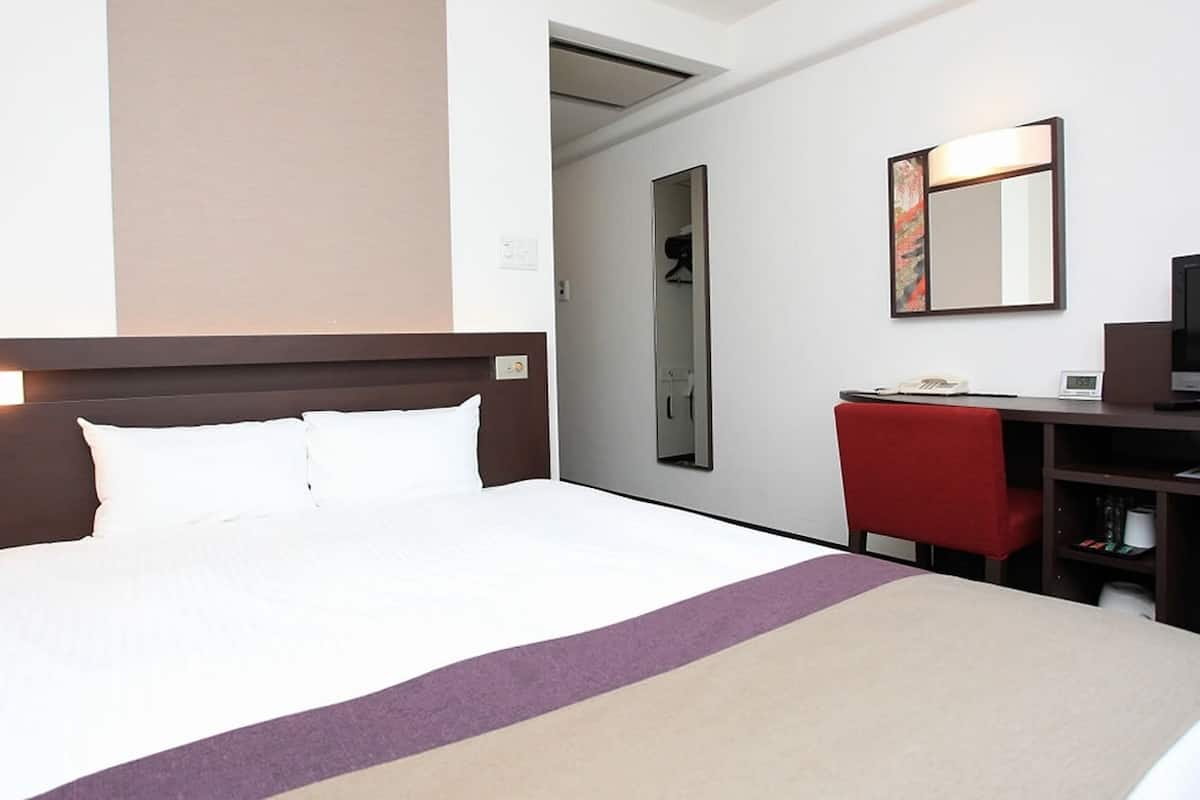 A hotel room with a large bed, a desk with a chair, a television, and a mirror.