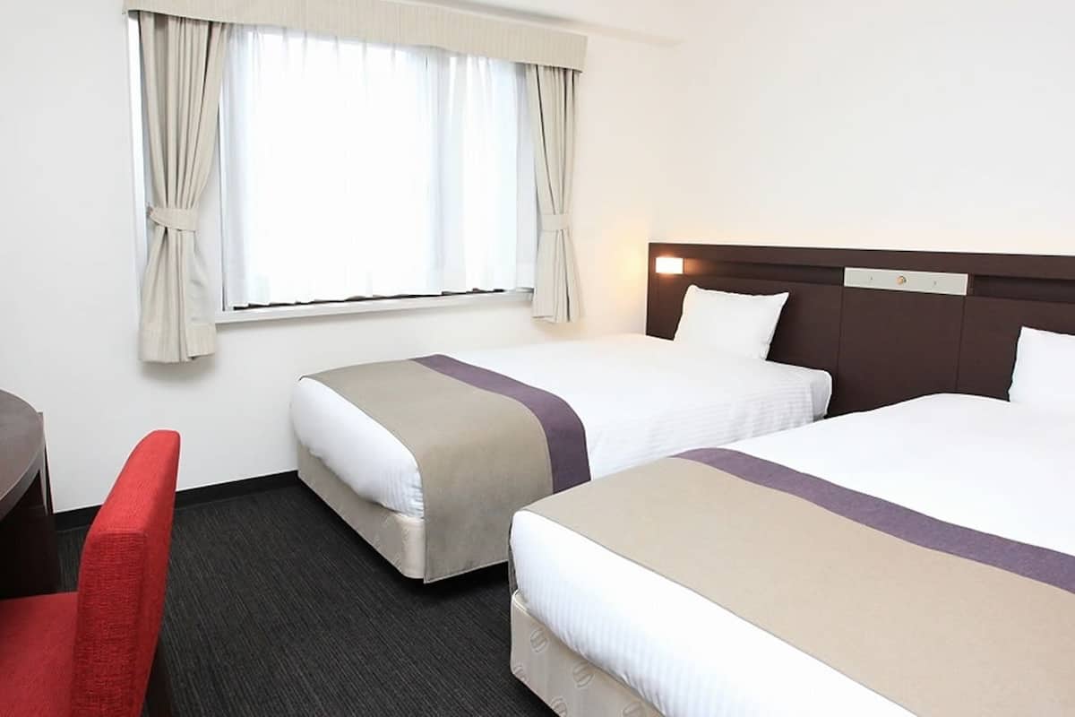 A hotel room with two beds, a desk, a television, and a window with curtains.