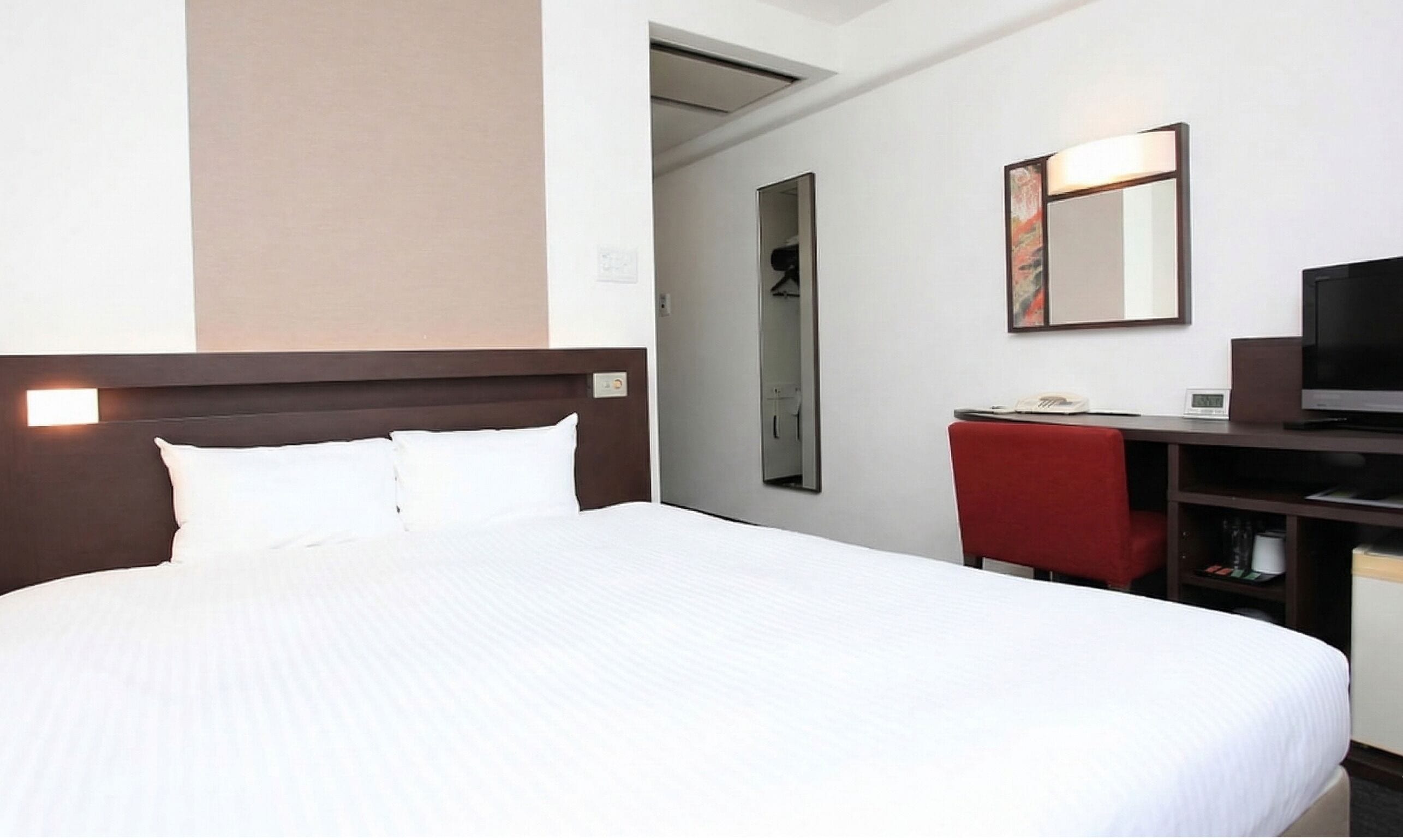 A hotel room with a large bed, a desk with a chair, a television, and a mirror.