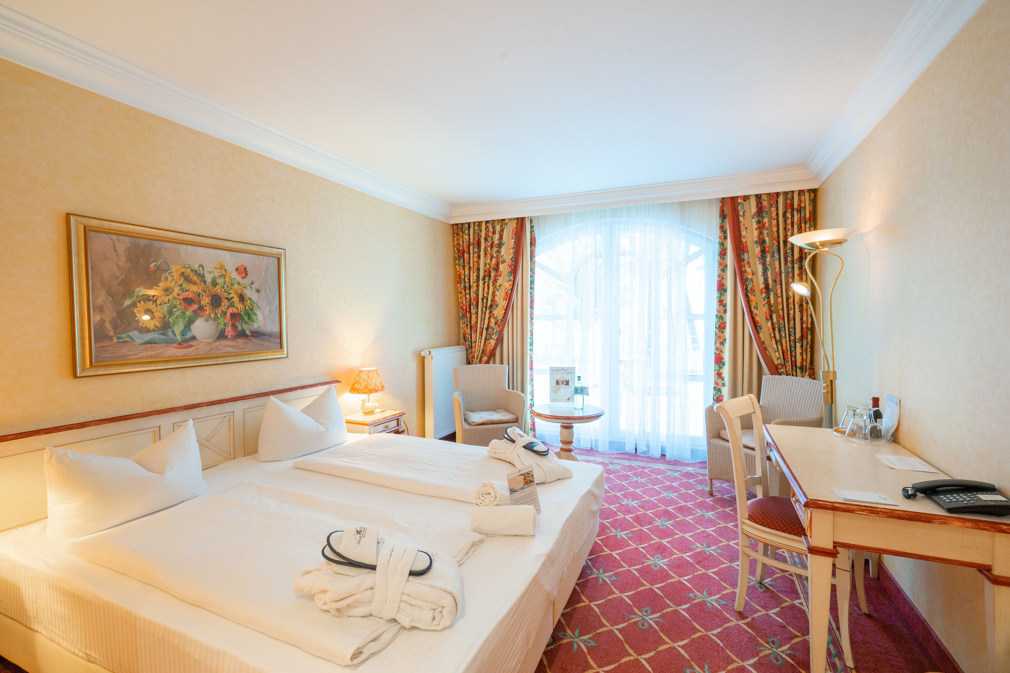 A hotel room with a large bed, a desk, a chair, a lamp, and a painting on the wall.