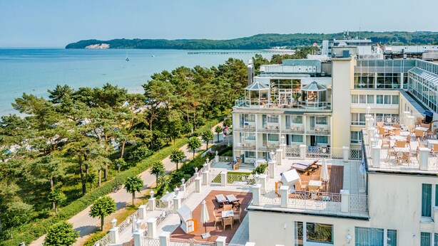 A hotel with multiple balconies overlooking a coastal area, featuring outdoor seating and a view of the sea. - Rugard Thermal Strandhotel (Binz)