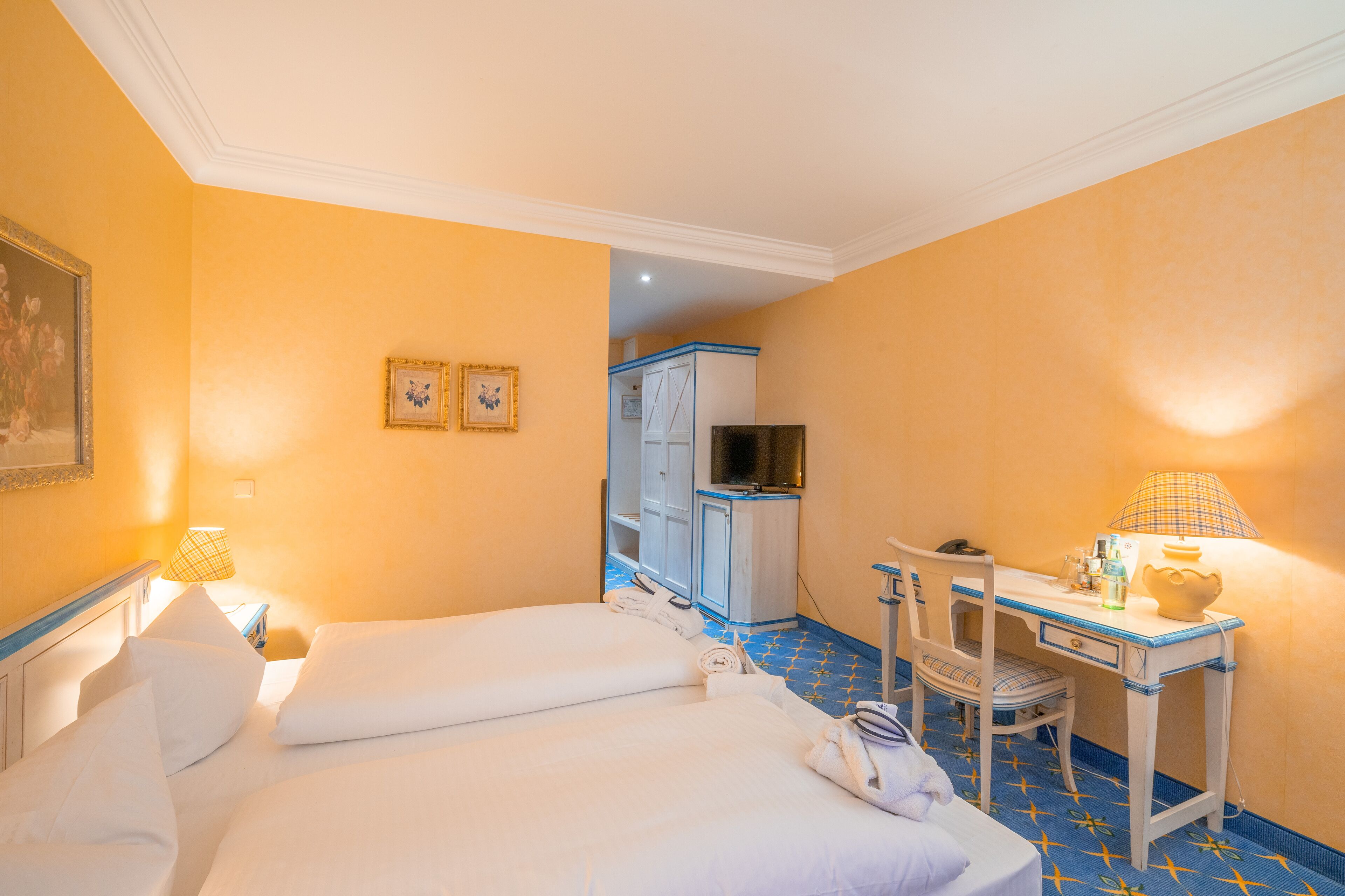 Ein Hotelzimmer mit zwei Betten, einem Schreibtisch, einem Stuhl, einer Lampe und einer Minibar.