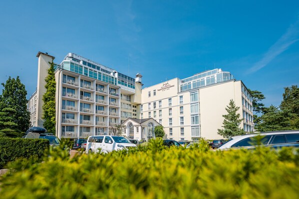 A multi-story hotel with a central courtyard, balconies, and a parking area.