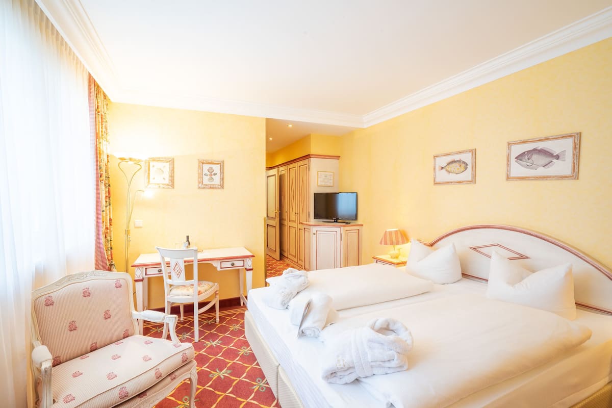 Une chambre d’hôtel avec un lit, un bureau, une chaise, une télévision et deux tableaux encadrés au mur.