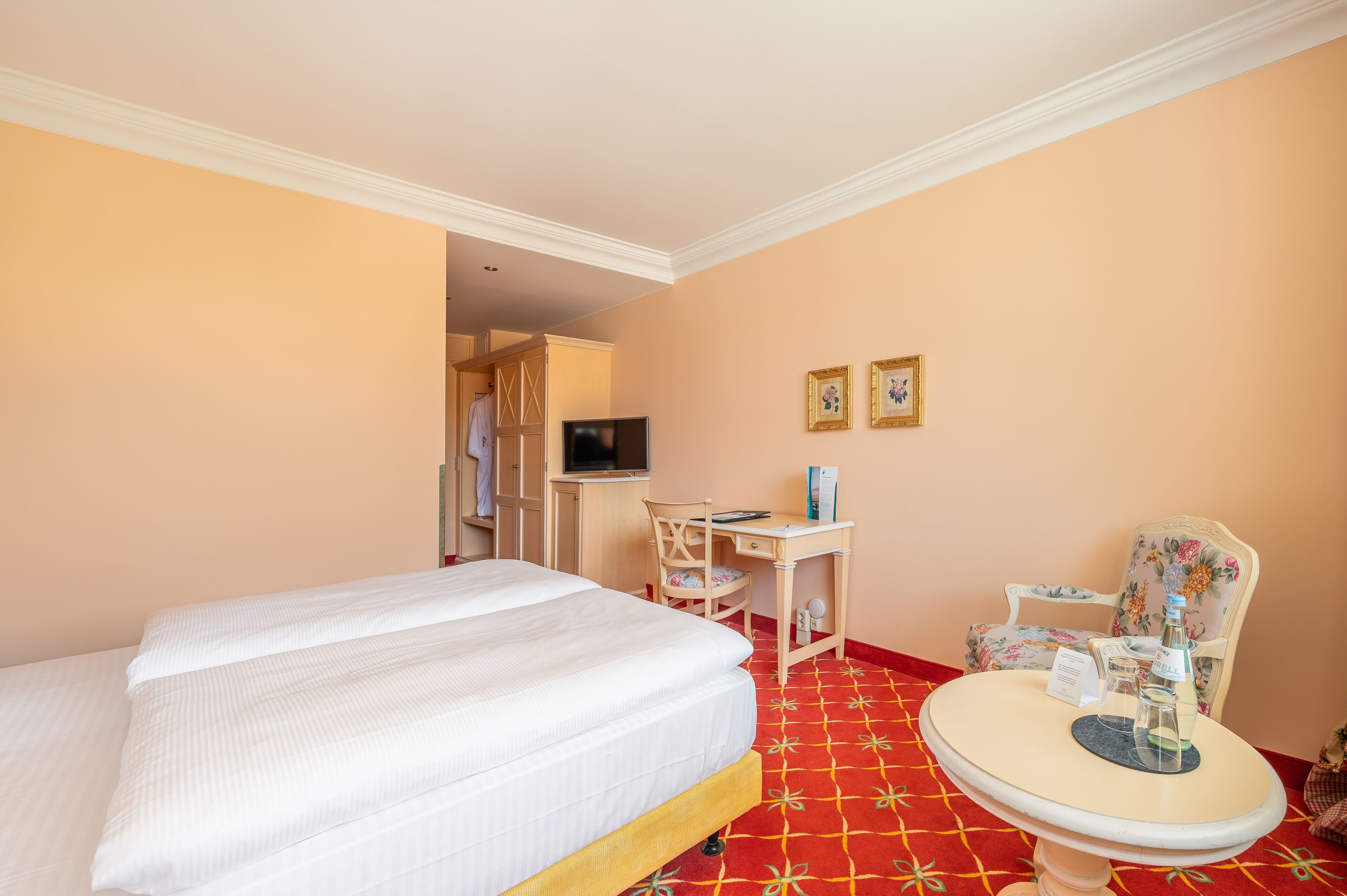 Una habitación de hotel con una cama, un escritorio, una silla, un televisor y una mesita con una botella y vasos.