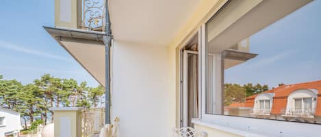 Un balcón con una mesa de vidrio y una silla blanca, con vistas a un césped verde y edificios vecinos.