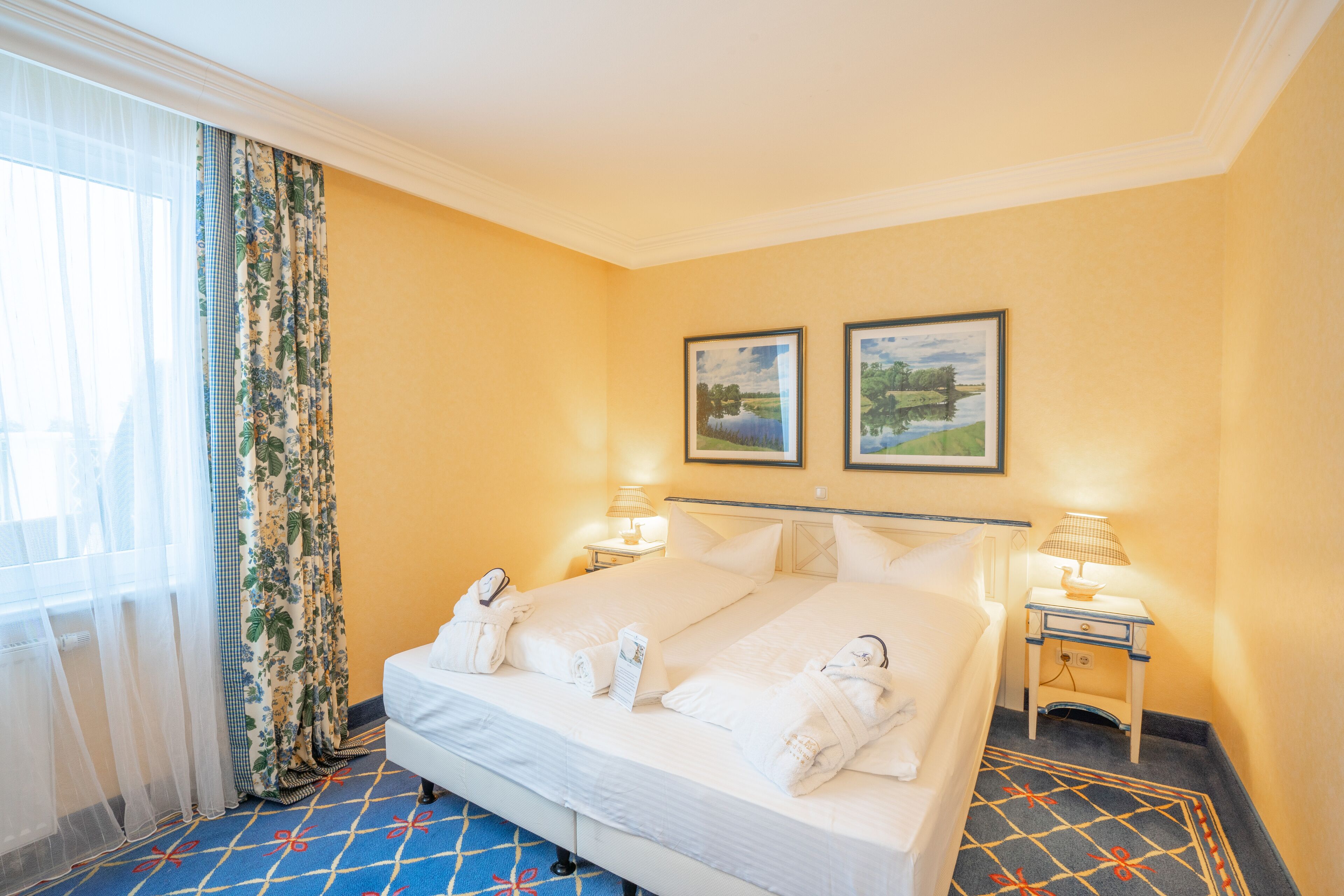 A hotel room with a large bed, two bedside lamps, a nightstand, and a window with curtains.