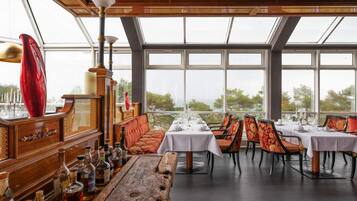 Ein Restaurant mit einer langen Holztresen, mehreren Esstischen und großen Fenstern mit Blick auf Bäume.