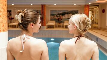 Two people in a swimming pool area with a view of a pool and a seating area in the background.
