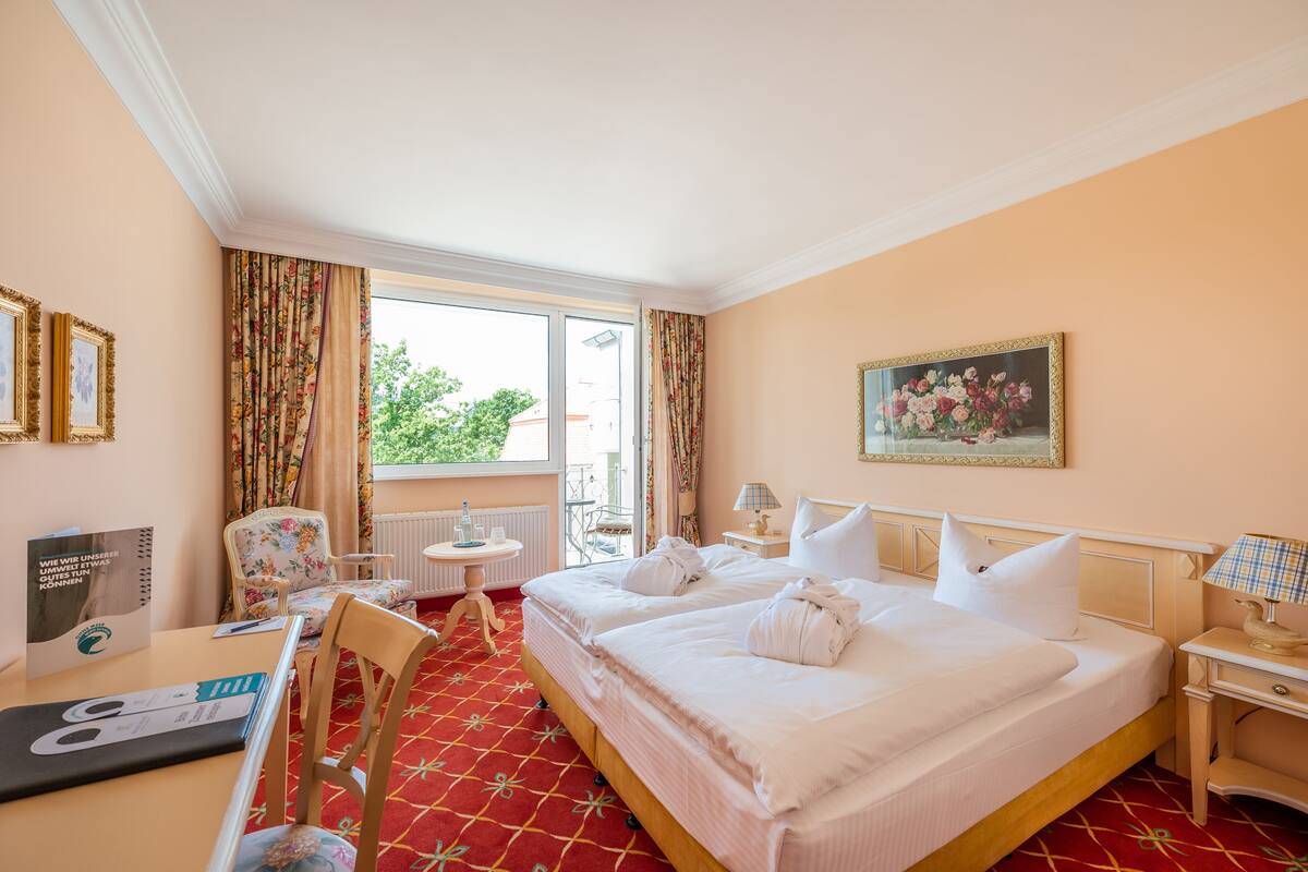 Une chambre d’hôtel avec un grand lit, un bureau avec un ordinateur portable, une chaise, une petite table et une fenêtre avec des rideaux.