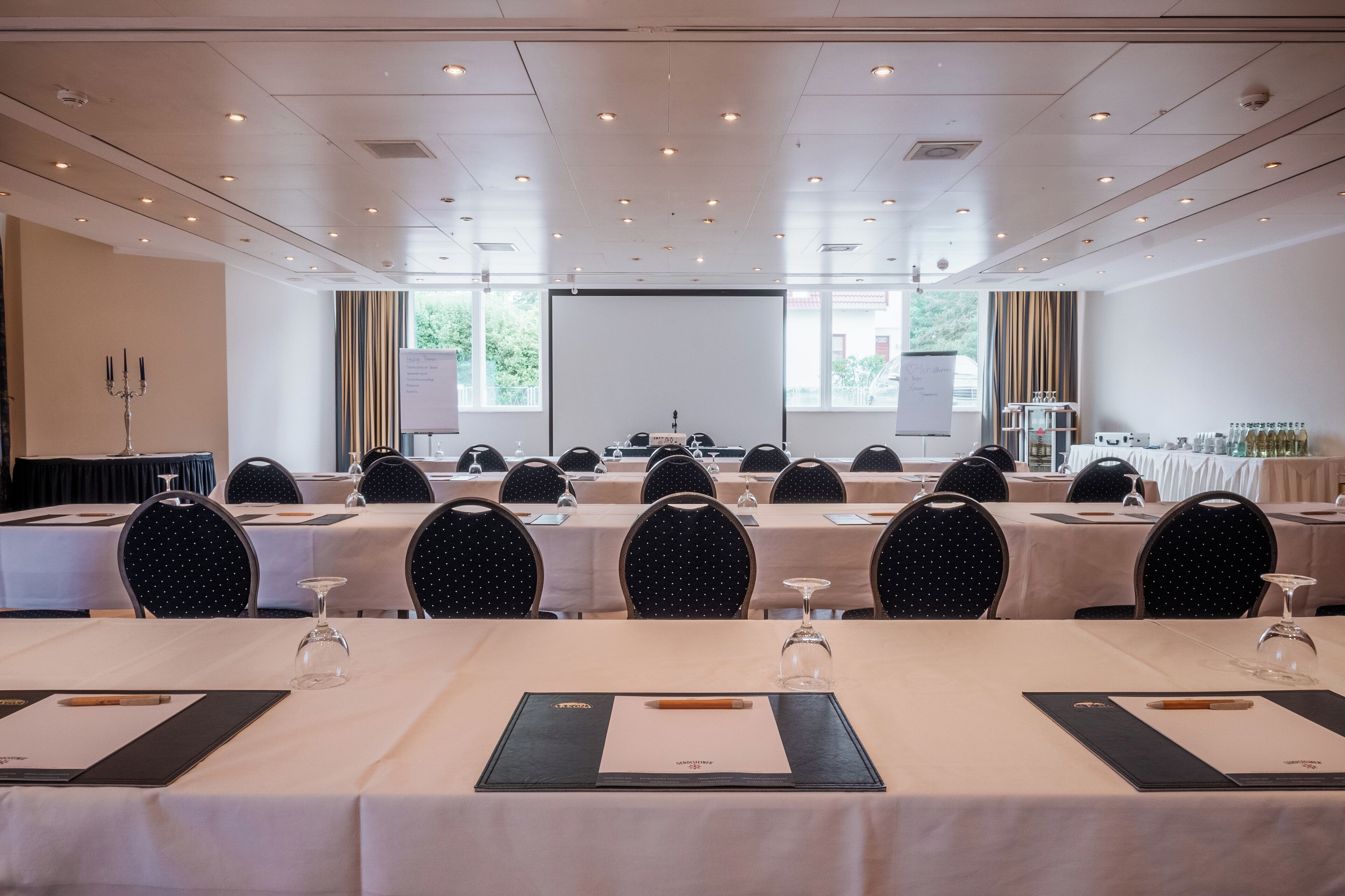 A conference room with multiple tables, chairs, and a projector screen.