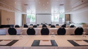 A conference room with multiple tables, chairs, and a projector screen.