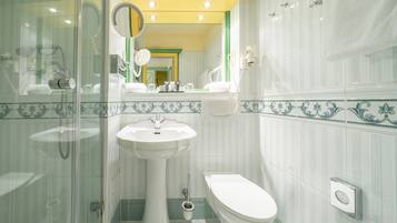 Ein Badezimmer mit Duschkabine aus Glas, einem Standwaschbecken, einer Toilette und einem Spiegel über dem Waschbecken.