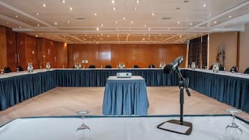 Un salón de conferencias con una mesa larga, un proyector y un micrófono.