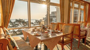 A dining area with a table set for four, overlooking a scenic view of the sea and buildings. - Rugard Thermal Strandhotel (Binz)