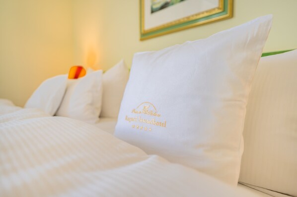Una cama bien hecha con sábanas y almohadas blancas, una de ellas con un logotipo y texto que indica el nombre de un hotel.