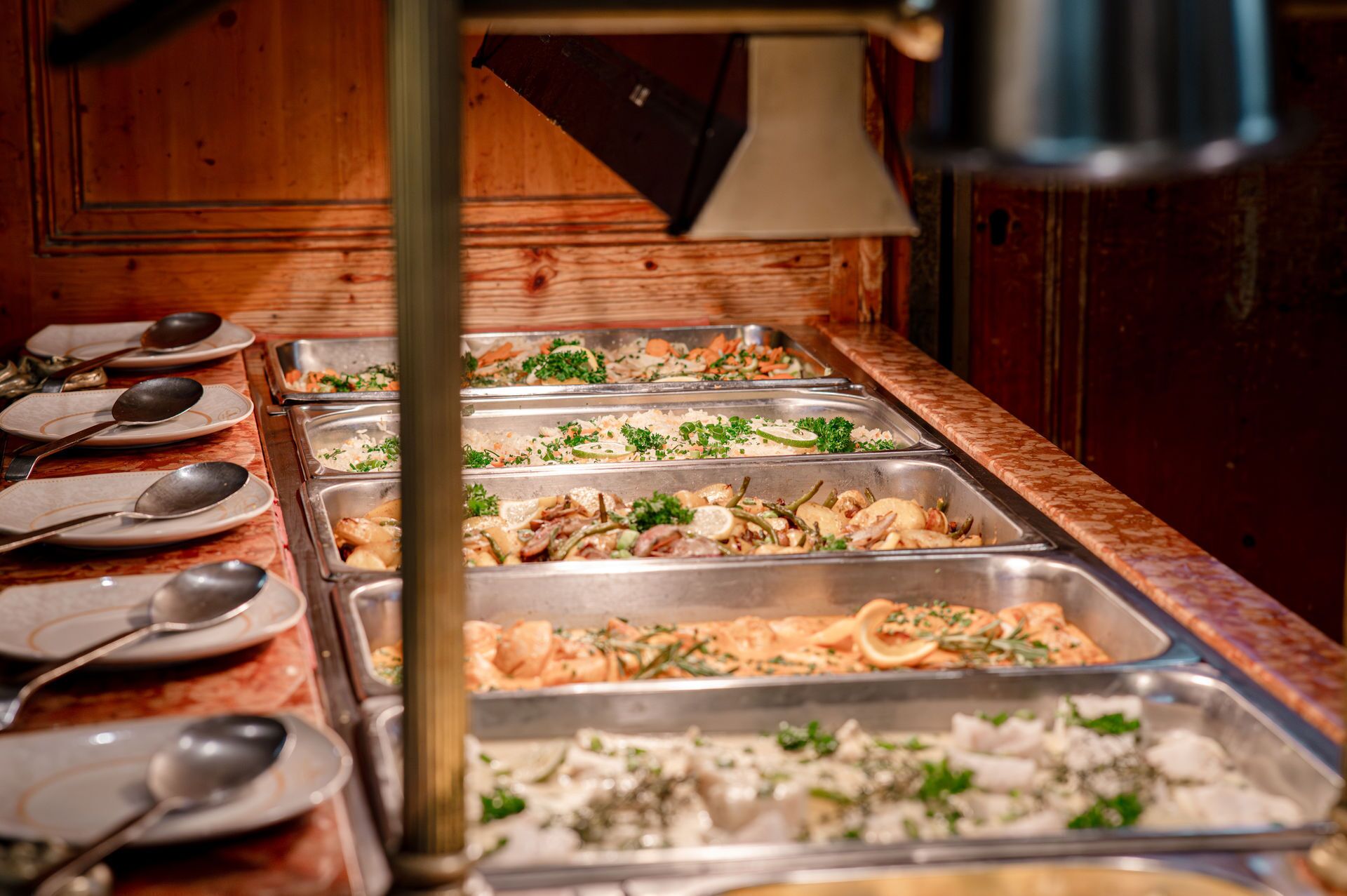 Buffet variado com diversos pratos, incluindo frutos do mar e vegetais, e vários utensílios de servir.