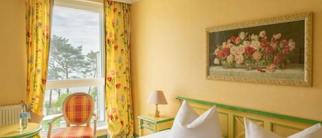 Habitación de hotel con cama, una silla, una mesa, una lámpara y un cuadro en la pared.