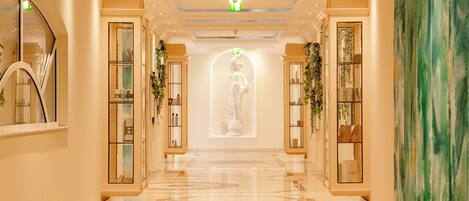 A hotel corridor with a marble floor, glass display cases, and a statue at the end.