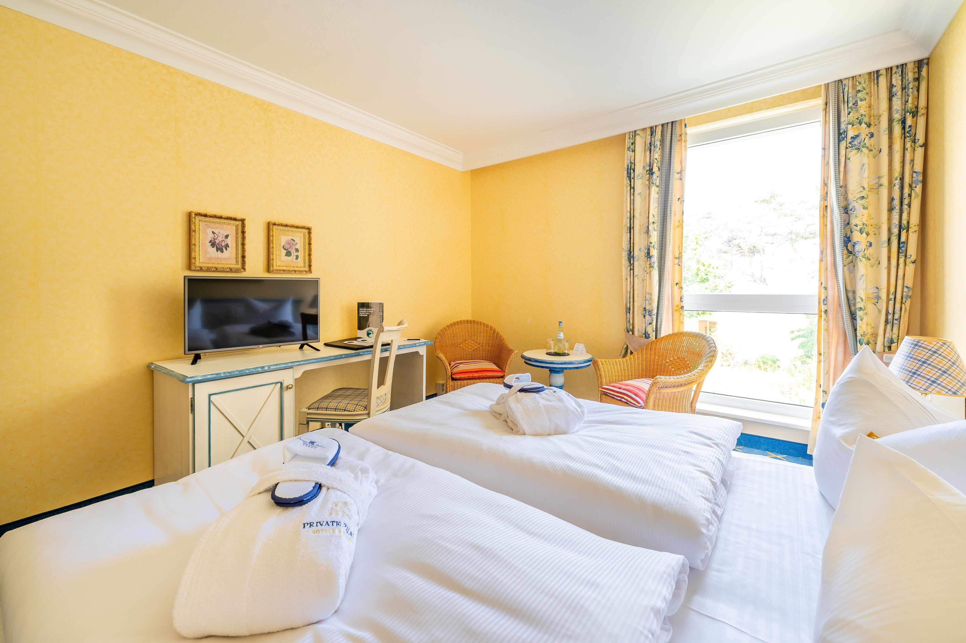 Habitación de hotel con dos camas, un televisor, un escritorio pequeño y una ventana con cortinas.