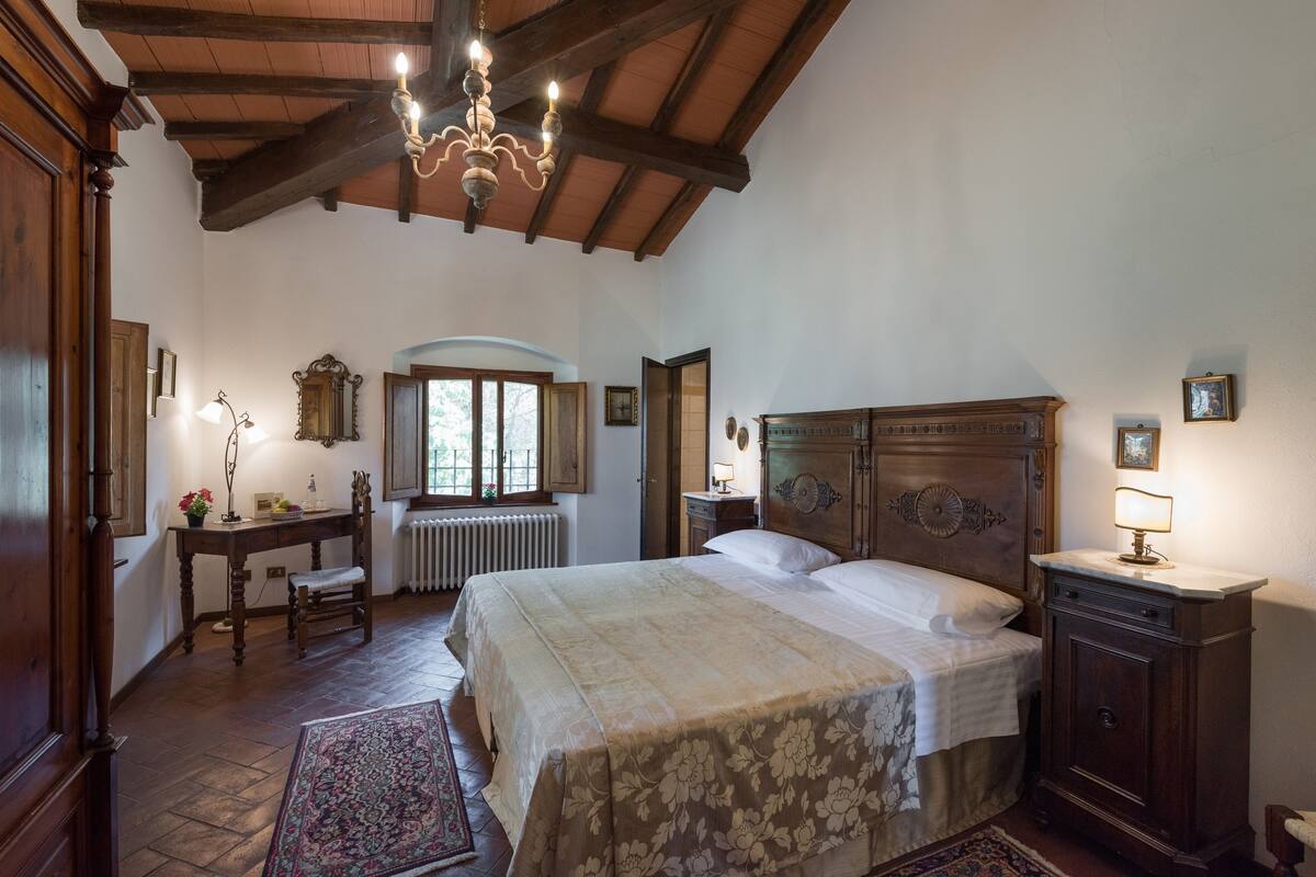 A bedroom with a large bed, wooden furniture, a chandelier, and a window with a view.