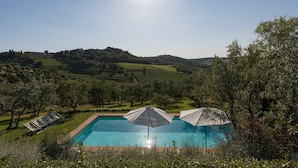 A pool with lounge chairs and umbrellas, surrounded by greenery and hills. - Relais Fattoria Valle (Greve in Chianti)