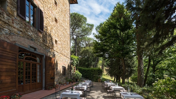 An outdoor dining area with tables and chairs, surrounded by greenery and a stone building. - Relais Fattoria Valle (Greve in Chianti)