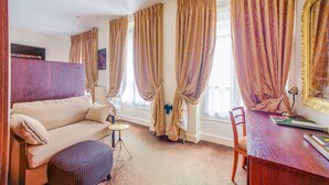 A room with a sofa, a small round table, a wooden desk, and a chair. - Queens Boutique Hotel (Paris)