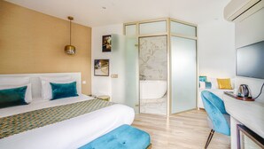 A modern hotel room with a large bed, a desk with a chair, a shower area, and a TV. - Queens Boutique Hotel (Paris)