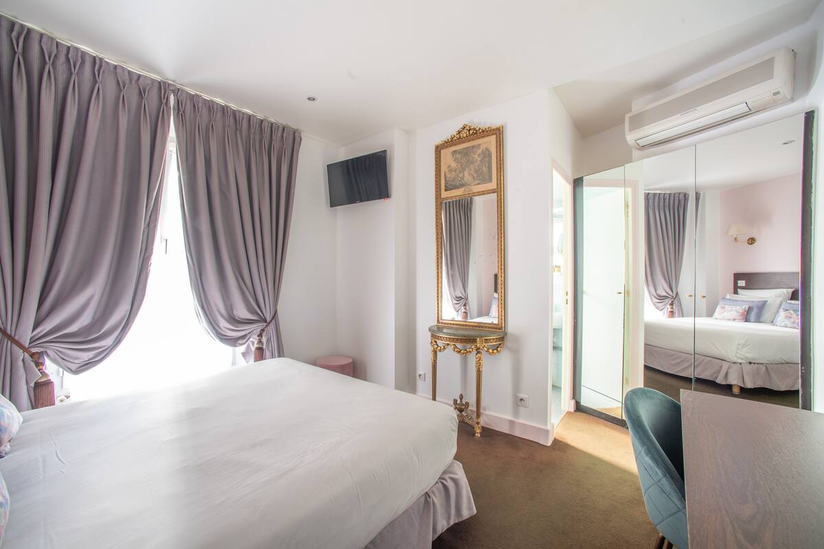 A hotel room with a large bed, a mirror, a TV, and a desk.