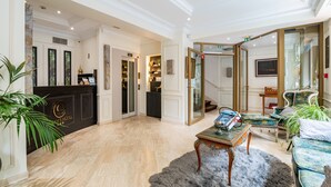 A spacious lobby with a marble floor, a reception desk, a plush fur rug, and a seating area with a table and chairs. - Queens Boutique Hotel (Paris)