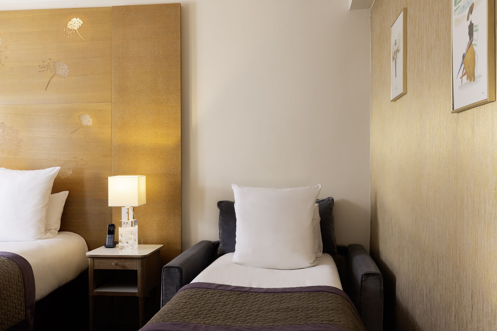 A hotel room with two beds, a nightstand with a lamp, and a wall with a textured panel and framed artwork.