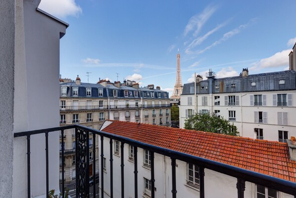 A view of the Eiffel Tower from a balcony with a red-tiled roof building in the foreground. - Hôtel Muguet (Paris)