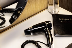 A black hairdryer, a black telephone, and a black book titled 'MUGUET' on a white surface. - Hôtel Muguet (Paris)