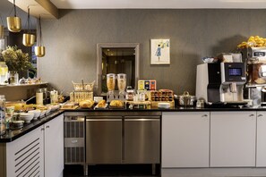 Una cocina industrial con electrodomésticos de acero inoxidable, una máquina de café y diversos alimentos sobre la encimera.