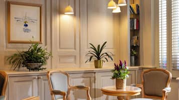A room with a wooden panel wall, a framed painting, a bookshelf, and two chairs around a small table.