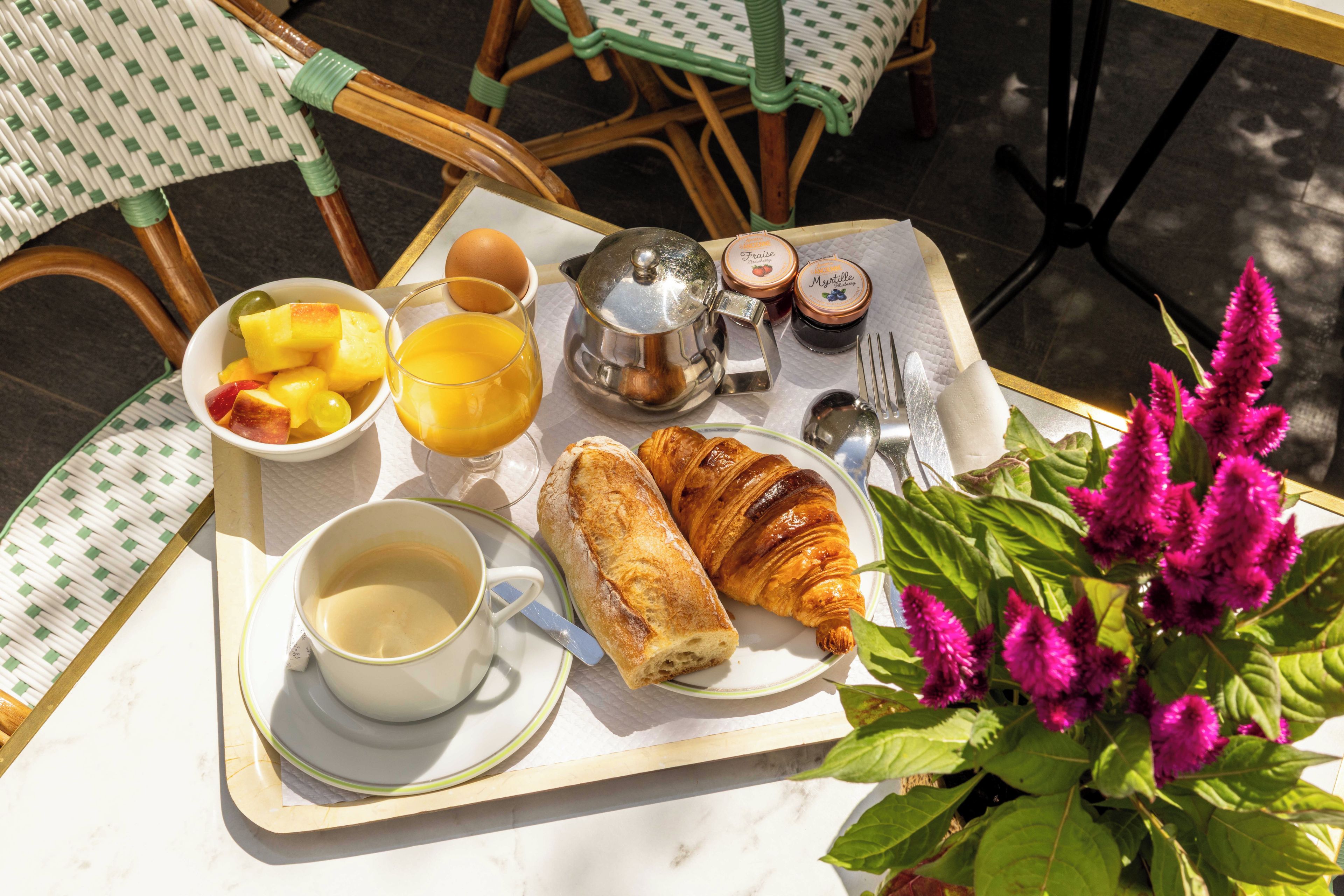 Bandeja de café da manhã com croissants, frutas, um copo de suco de laranja, xícara de café e acompanhamentos.