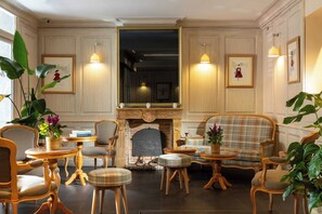 A classic interior with a fireplace, wooden furniture, and framed artwork. - Hôtel Muguet (Paris)