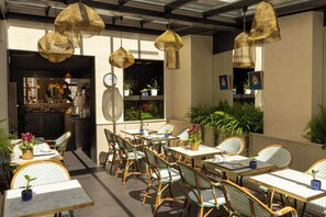 An outdoor café area with wicker furniture, hanging lights, and potted plants. - Hôtel Muguet (Paris)