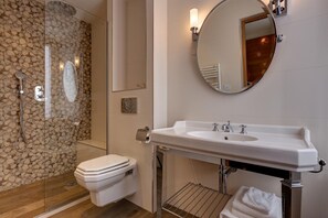 A modern bathroom with a stone wall shower, a white toilet, a large sink with a mirror, and a towel rack. - Hôtel Muguet (Paris)
