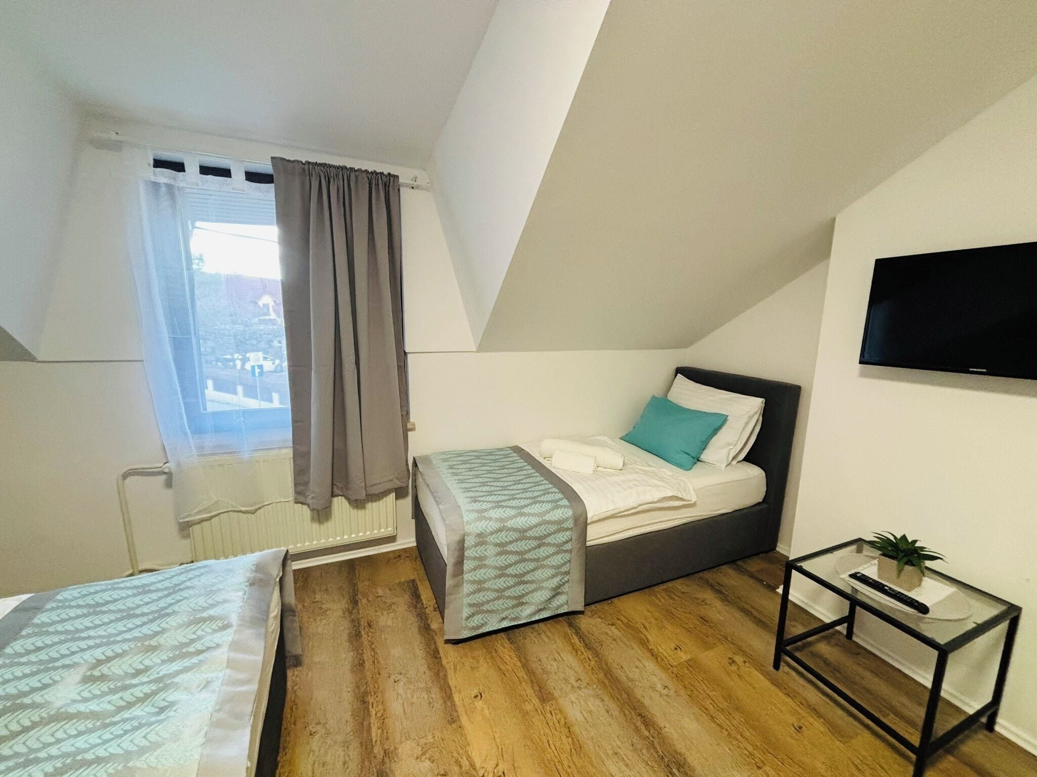 Un dormitorio pequeño y moderno con una cama individual, un televisor montado en la pared y una mesita con una planta.