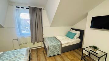 Un dormitorio pequeño y moderno con una cama individual, un televisor montado en la pared y una mesita con una planta.