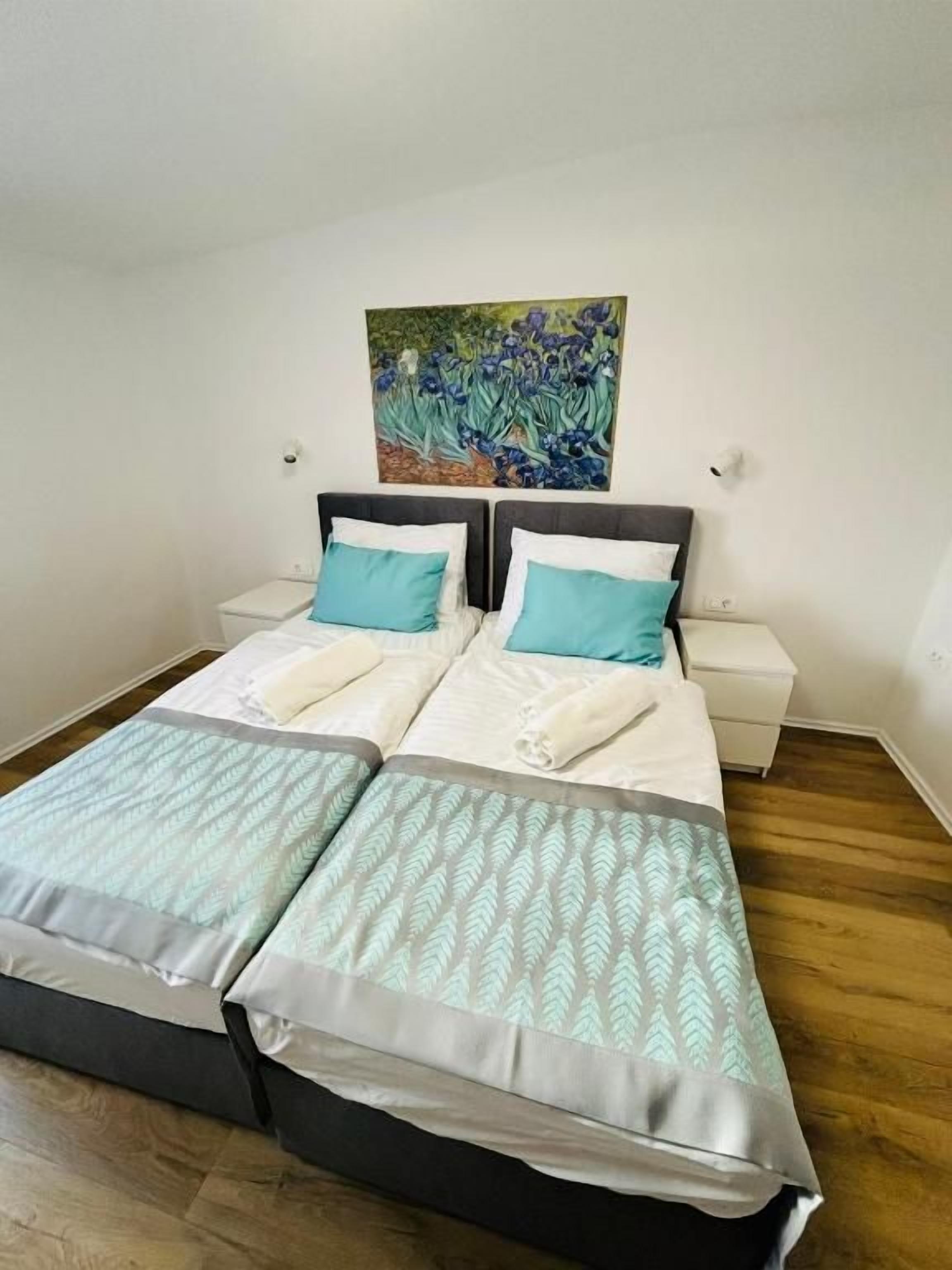 A double bed with a patterned bedspread, two pillows, a nightstand, and a wall-mounted painting.
