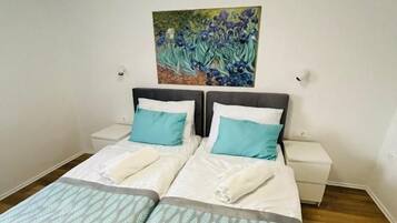 A double bed with a patterned bedspread, two pillows, a nightstand, and a wall-mounted painting.