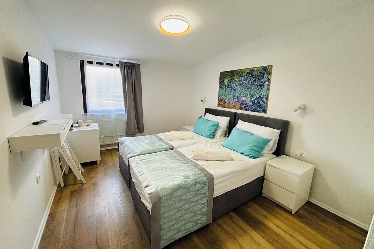 A bedroom with a bed, bedside tables, a desk, a TV, and a window with curtains.